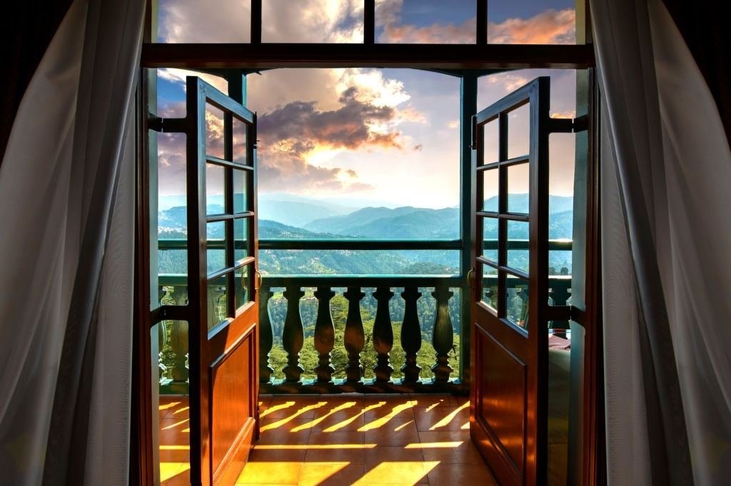 Balcony doors opening to a view of the Dharamshala hills at sunset