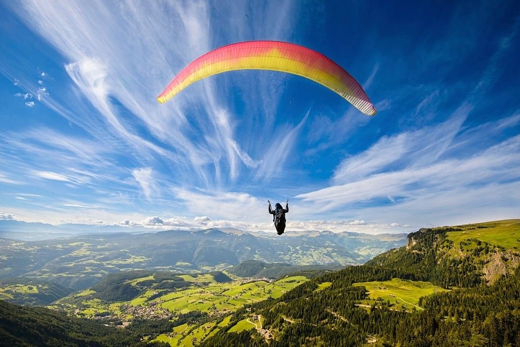 A paraglider flying over a green mountain valley
